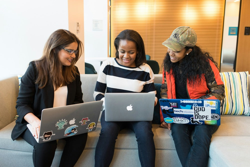 image of three ladies seated with laptops on their laps 