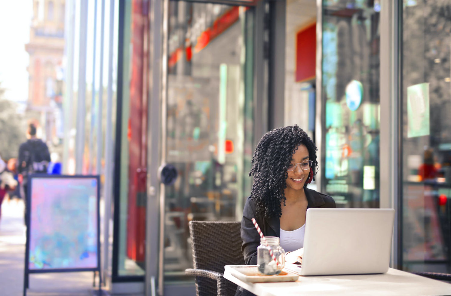 Black woman freelancer working outside of a cafe in a city. Learn how digital business cards are the best option for freelancers.