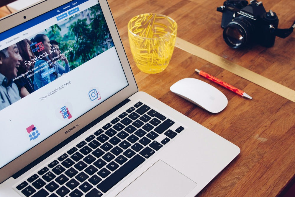 An image of a laptop placed on a table next to a glass and camera